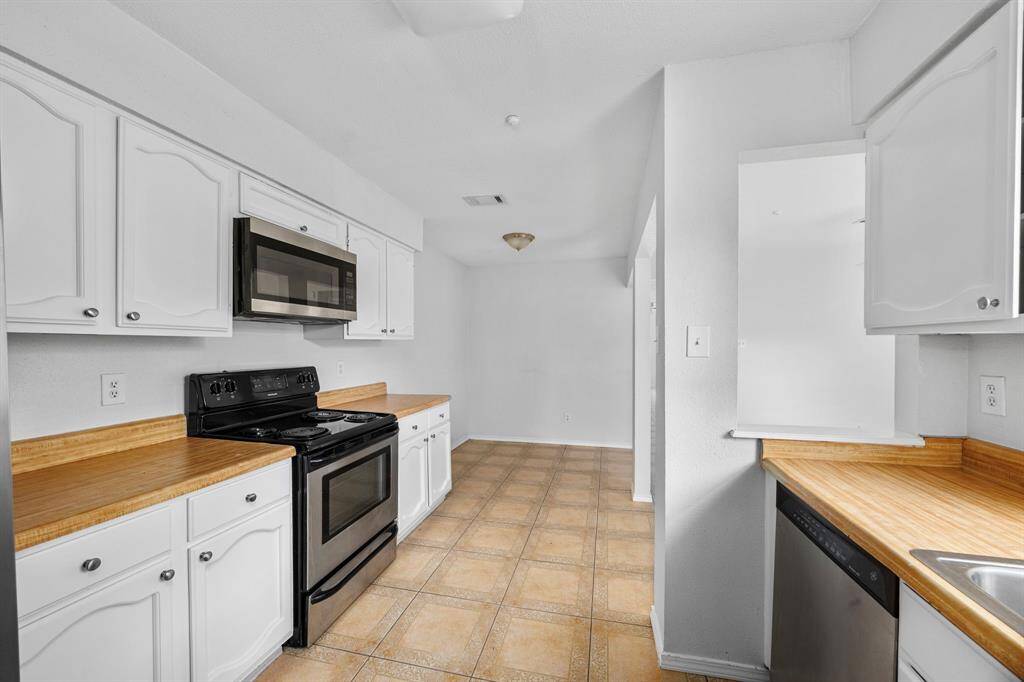 Bright kitchen with white cabinets, wood countertops, and tile flooring. Equipped with modern black appliances, including a stove and microwave. Ample natural light and open layout enhance the space.