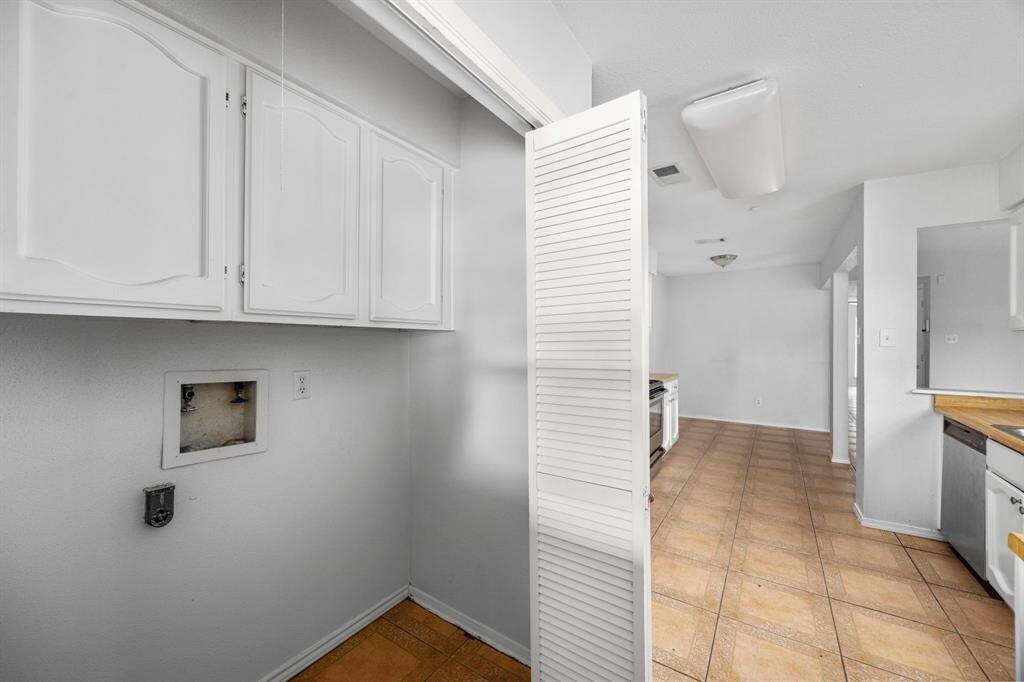 This photo shows a bright laundry area with white cabinetry and tiled flooring, leading into a spacious kitchen with ample counter space and modern lighting.
