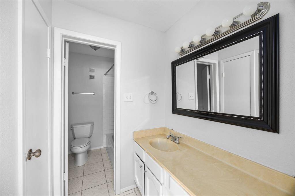 This bathroom features a spacious vanity with a large mirror and ample lighting. It includes a separate toilet and shower area with white tile, offering a clean and bright space.