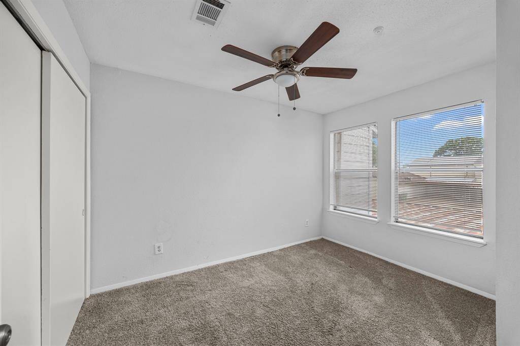 This bright and airy room features neutral carpeting, a ceiling fan, and large windows with blinds, offering plenty of natural light. The space is versatile and ideal for a bedroom or office.