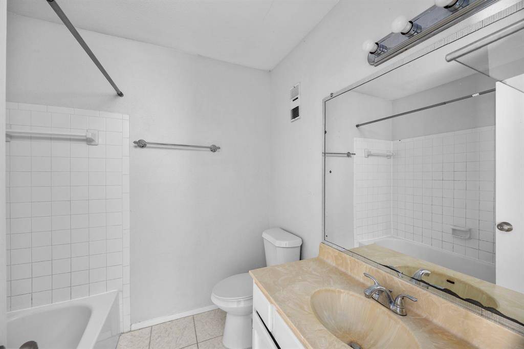 This bathroom features a clean, bright design with a combination shower and bathtub, a large mirror, single vanity with a light-colored countertop, and tiled flooring.