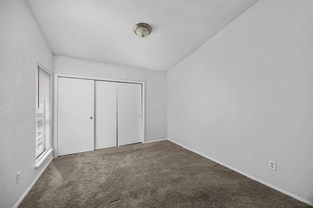 This room features a vaulted ceiling, neutral walls, and carpeted flooring. It includes a window for natural light and a closet with sliding doors. Ideal for a bedroom or office space.