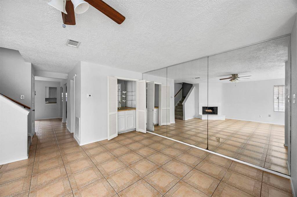 This spacious living area features tiled floors, a mirrored wall enhancing the room's depth, a built-in cabinet, and a cozy fireplace. The ceiling fan adds comfort, while the open layout connects to other areas of the home.