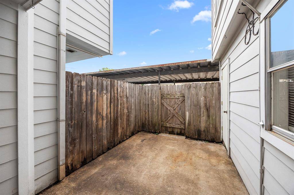 A small, enclosed outdoor area with concrete flooring is surrounded by wooden fencing. The space is bordered by white siding from the house and features a simple wooden gate. Ideal for a private patio or storage.