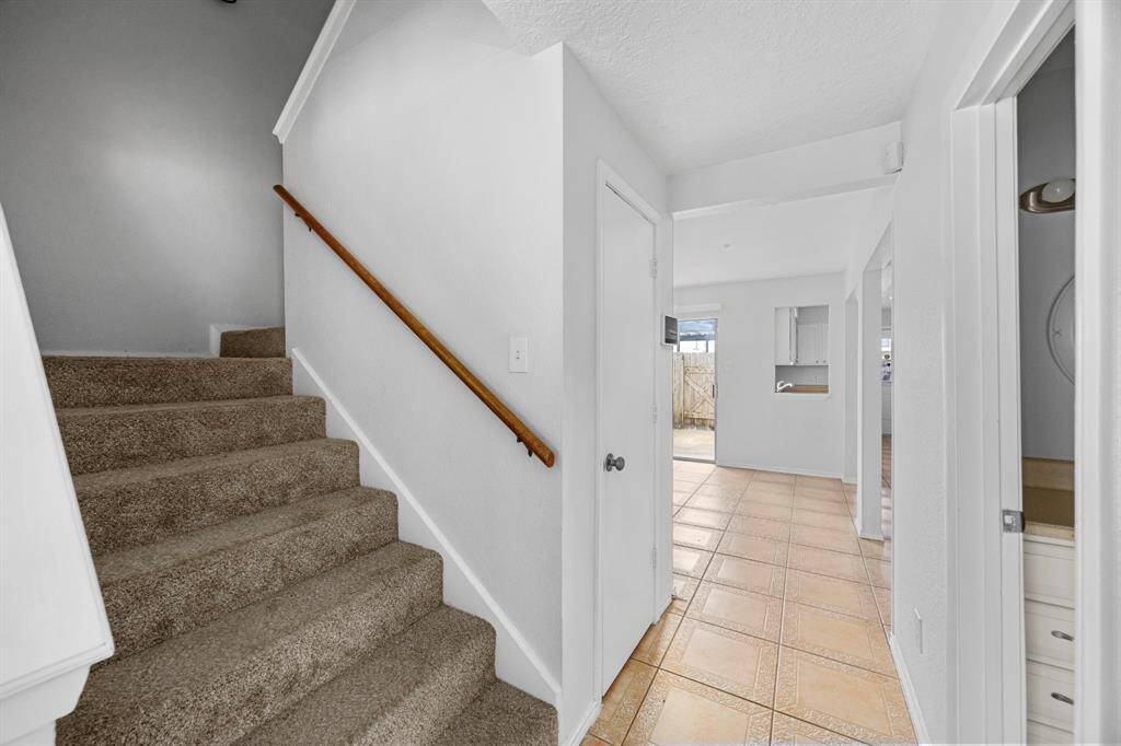 Bright entryway with tiled floors, carpeted stairs, and access to a kitchen area. Neutral walls and ample natural light create an inviting atmosphere.