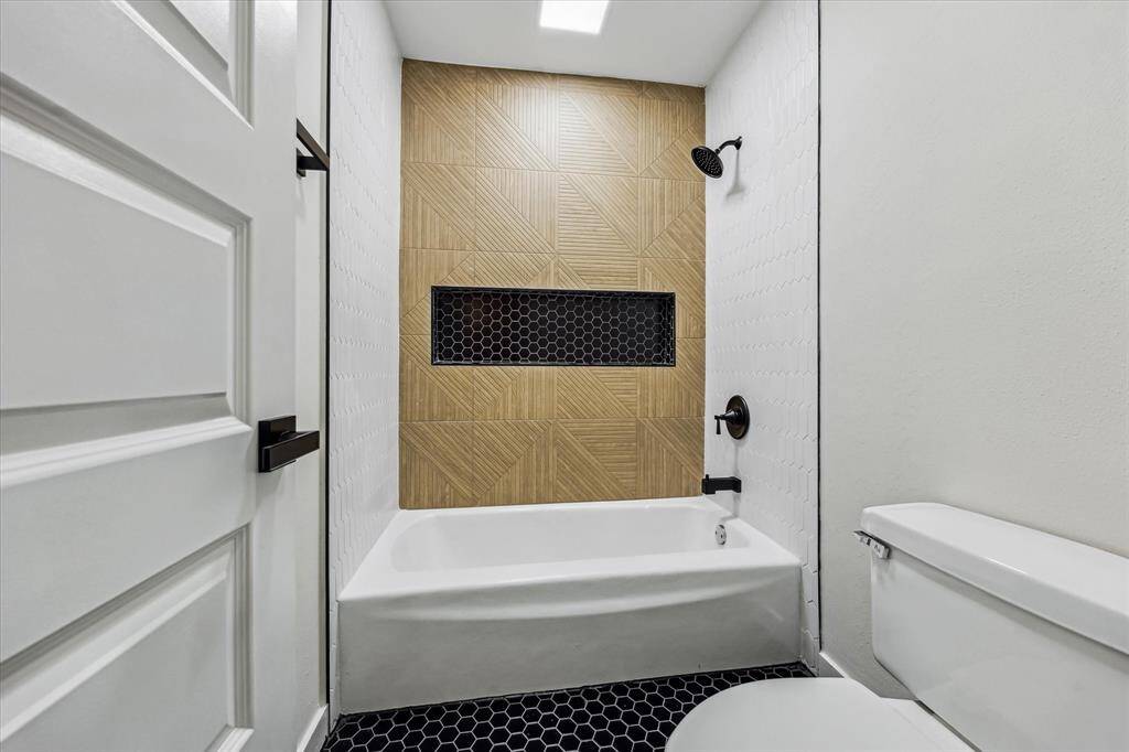Tub/shower combo with statement tile, black fixtures, and niche shelving