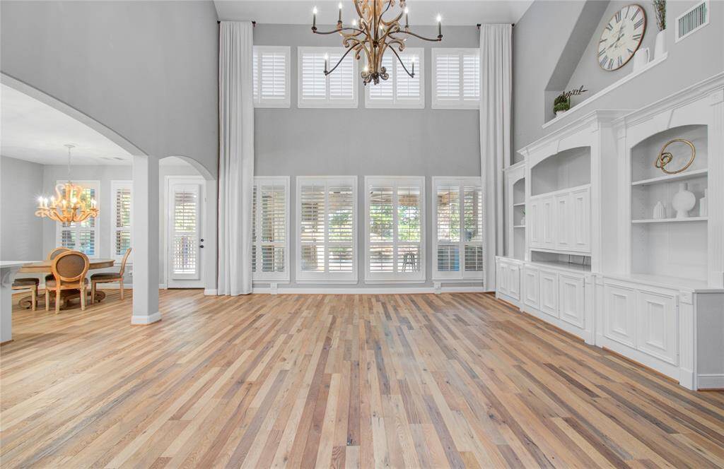 Spacious living area with high ceilings and large windows, providing ample natural light. The room features hardwood floors and a built-in white entertainment center.
