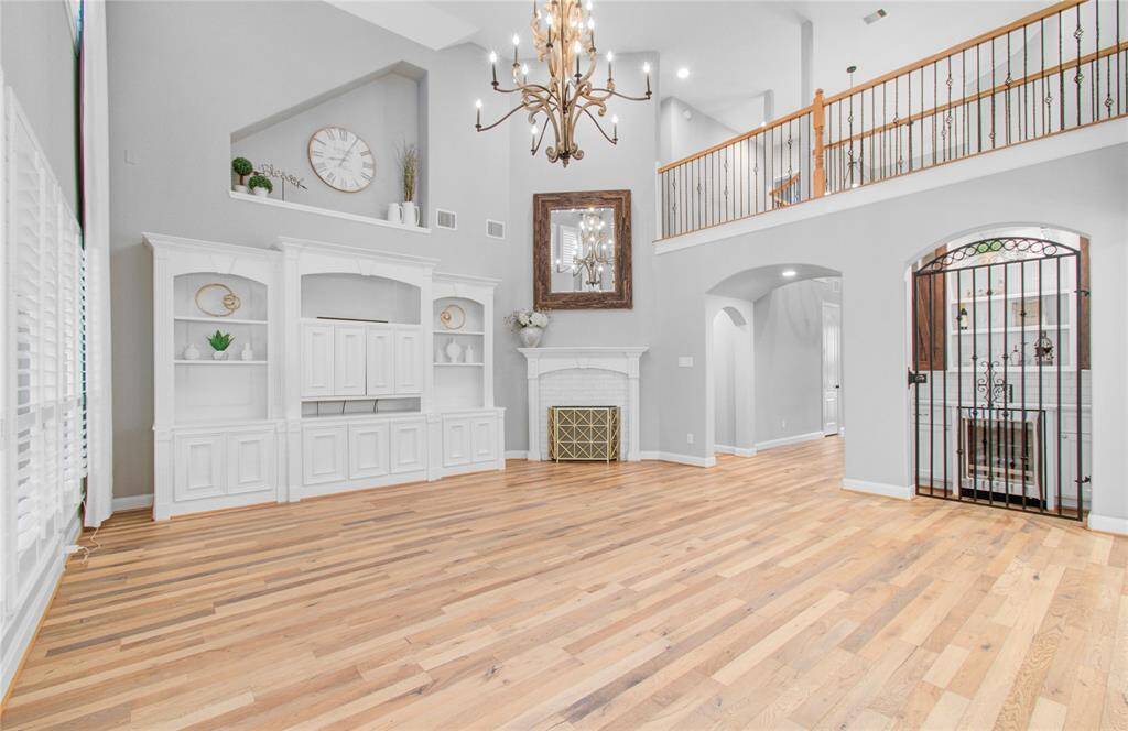 This spacious living area features high ceilings, elegant hardwood floors, and a grand resort style chandelier. A gas fireplace, built-in shelving, and a decorative iron gate adds character to wine grotto.