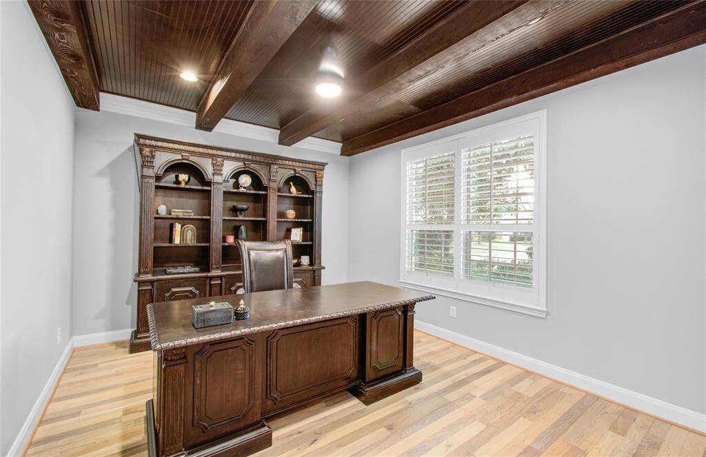 Stylish home office features decorative wooden beams on the ceiling, large window with white shutters, offering a bright and elegant workspace.