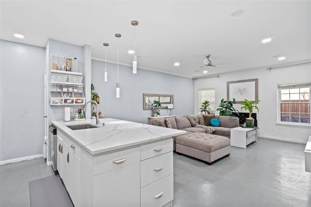 This beautifully designed open-concept space seamlessly blends the kitchen and living area, creating an inviting atmosphere for both cooking and entertaining. The sleek white island with a waterfall quartz countertop serves as a focal point, complemented by elegant pendant lighting. The spacious living area features a plush sectional sofa, large windows for natural light, and modern finishes, making it the perfect space to relax and unwind.