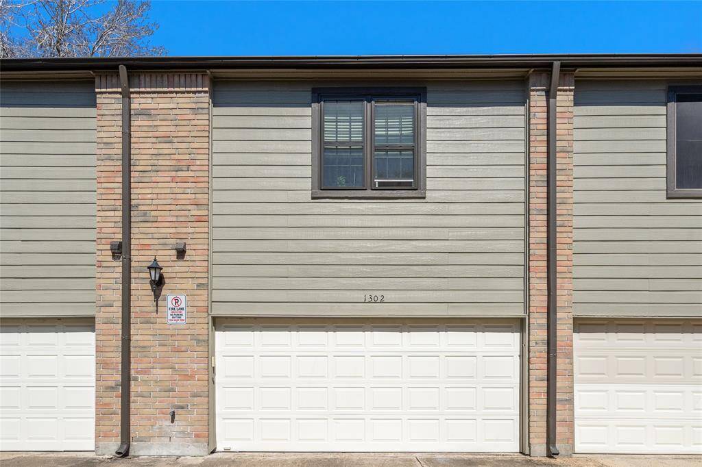 The rear of 9850 Pagewood Lane #1302 features a spacious two-car garage with a crisp white door, offering convenience and security. A blend of brick and modern siding gives the exterior a timeless yet updated look. The upper-level window allows for natural light, enhancing the home's inviting feel. A well-lit entry and clearly marked address add to the functionality of this charming townhome.