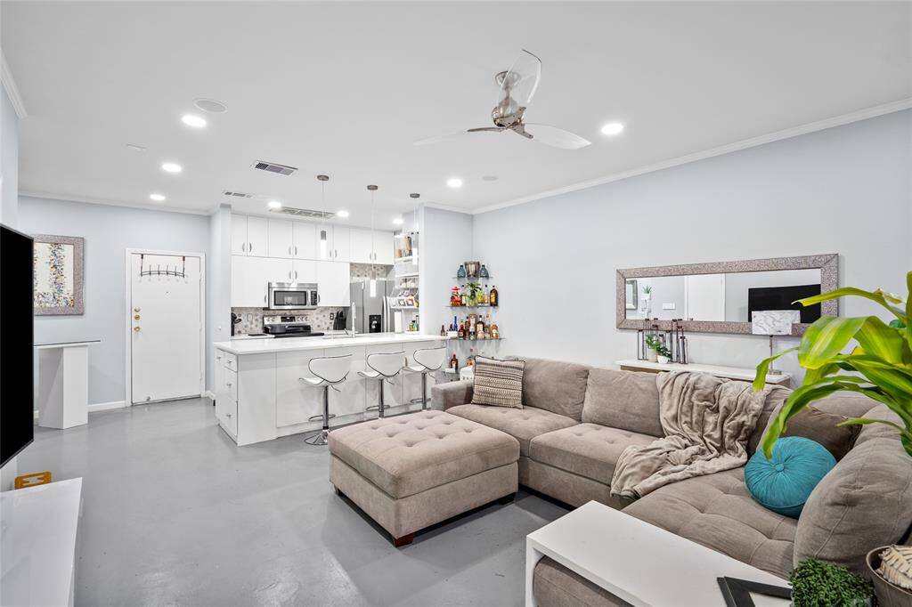 This beautifully designed open-concept space seamlessly blends the kitchen and living area, creating an inviting atmosphere for both cooking and entertaining. The sleek white island with a waterfall quartz countertop serves as a focal point, complemented by elegant pendant lighting. The spacious living area features a plush sectional sofa, large windows for natural light, and modern finishes, making it the perfect space to relax and unwind.