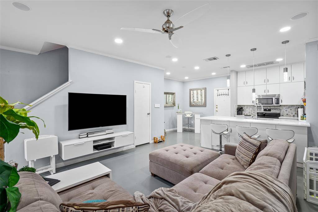 This beautifully designed open-concept living space seamlessly connects to the modern kitchen, creating an ideal layout for both relaxation and entertaining. The spacious living area features recessed lighting, a sleek ceiling fan, and a neutral color palette that enhances the home's contemporary feel. The kitchen boasts crisp white cabinetry, stylish pendant lighting, and a large island with bar seating—perfect for casual dining or gathering with guests.