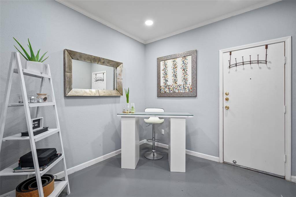 This inviting entryway doubles as a sleek and modern workspace. Love how the owners designed this area featuring a glass-top desk, a contemporary white barstool, and a decorative ladder shelf for stylish storage. Soft gray walls complement the rustic wood-framed mirror and abstract artwork, creating a welcoming and functional space.