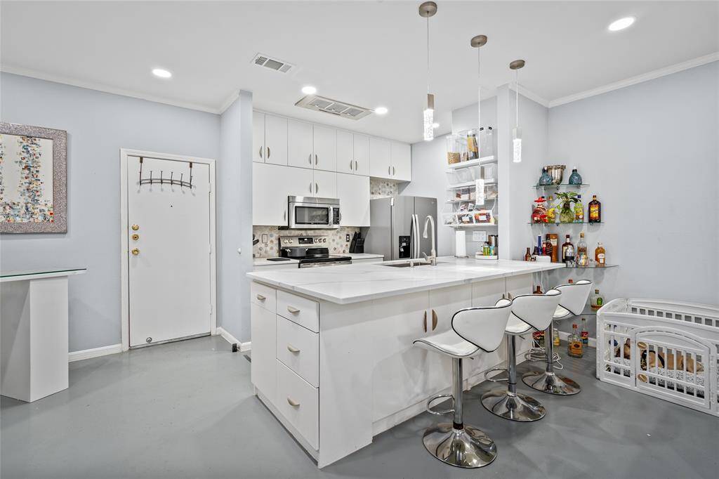 This stylish and functional kitchen features sleek white cabinetry, stainless steel appliances, and a stunning quartz countertop island with a breakfast bar. Pendant lighting adds a contemporary touch, while open shelving provides convenient storage. The adjacent bar area offers additional space for entertaining, making this kitchen perfect for hosting and everyday living.