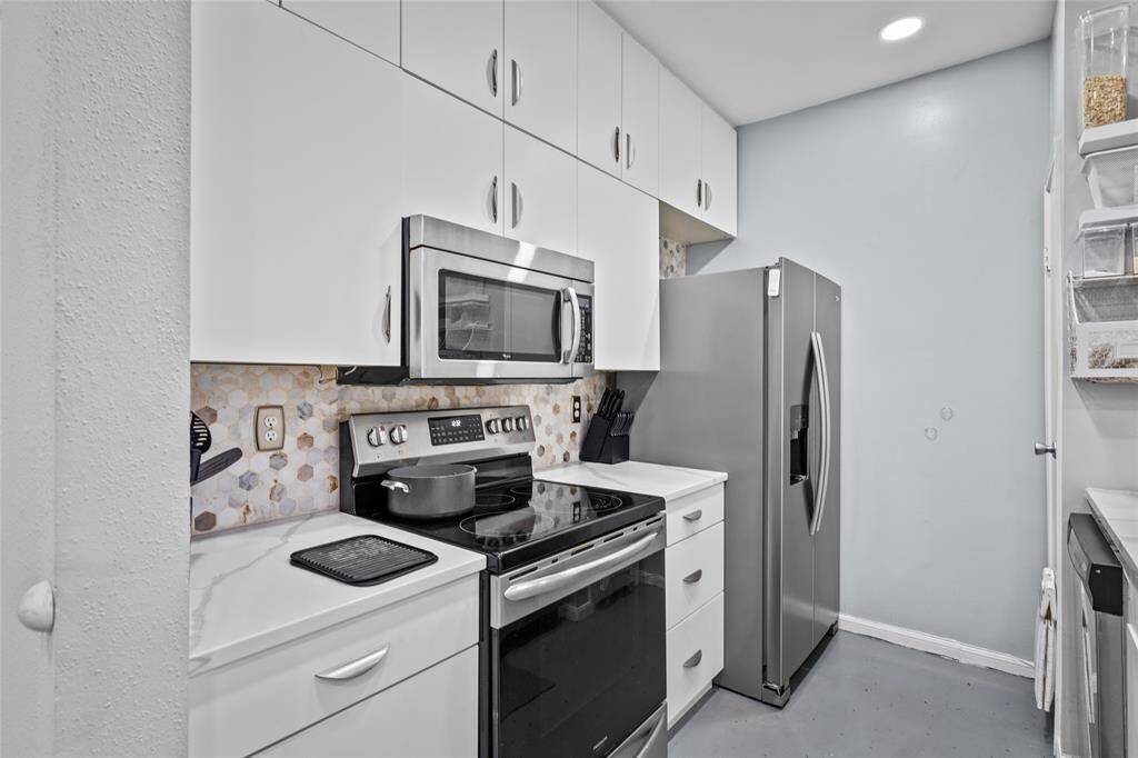 This compact yet highly functional kitchen showcases crisp white cabinetry, a stylish hexagonal backsplash, and quartz countertops. Stainless steel appliances—including a microwave, electric range, and spacious refrigerator—provide modern convenience, while ample overhead cabinets maximize storage. The clean, streamlined design makes meal prep and cooking a breeze.