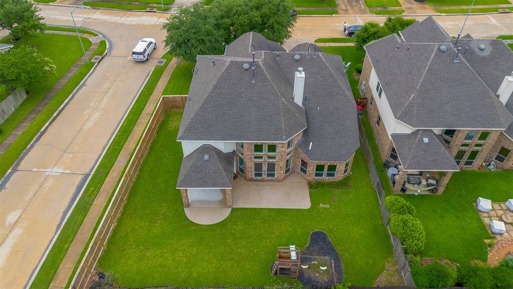 This aerial photo showcases a spacious two-story home with a large backyard, featuring a covered patio. The house is located on a corner lot in a well-maintained neighborhood, offering ample green space and privacy.