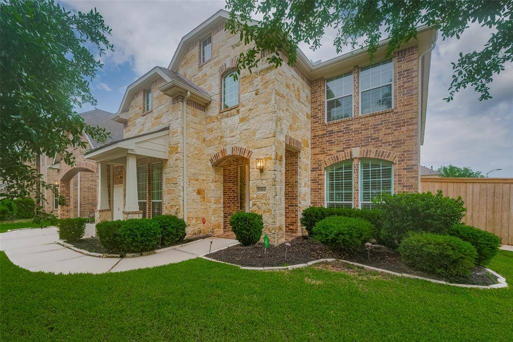 This inviting home features a two-story brick and stone exterior with well-maintained landscaping. A welcoming front porch and large windows enhance its curb appeal, all set against a neatly manicured lawn.
