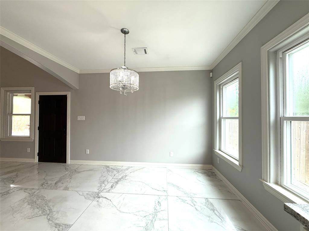 Bright and elegant breakfast room with large windows, gray walls, and marble-like flooring. Features a modern chandelier and crown molding, offering a sophisticated and airy atmosphere.