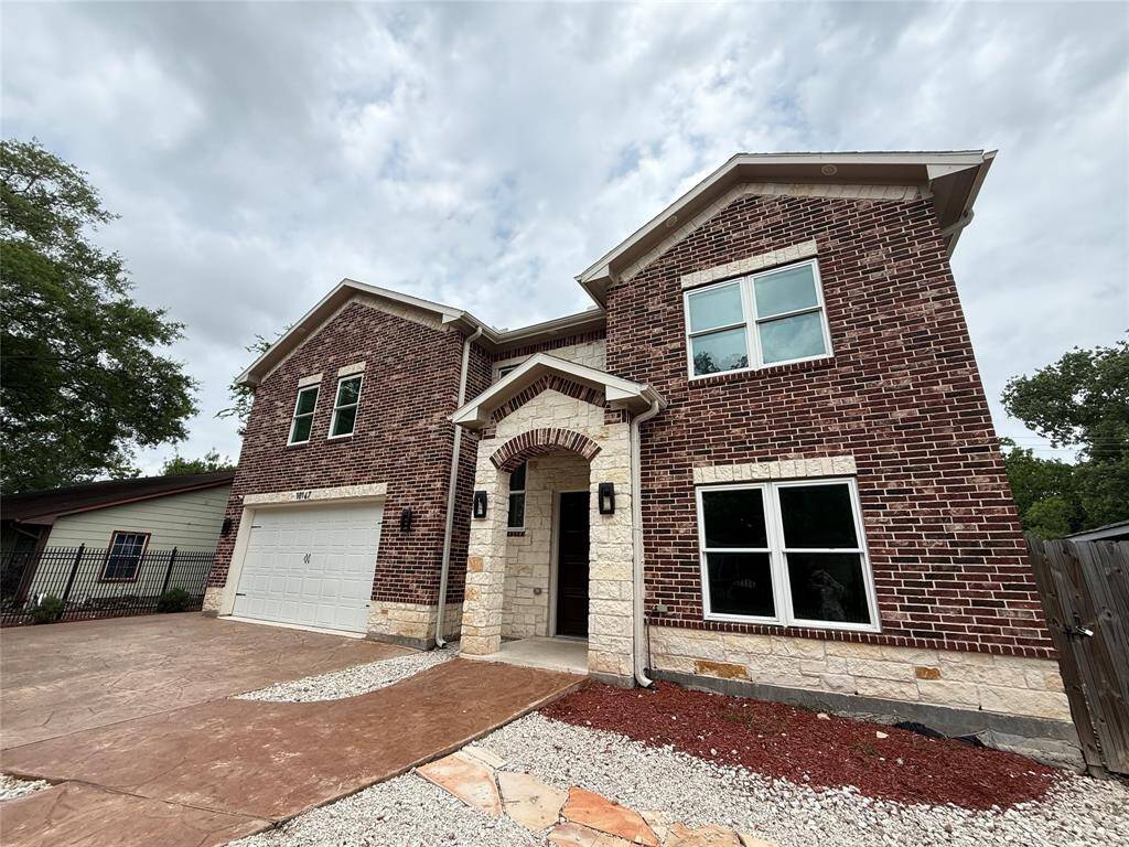 This is a two-story brick home with a modern design, featuring a two-car garage, large windows for ample natural light, and a landscaped front yard with stone accents.