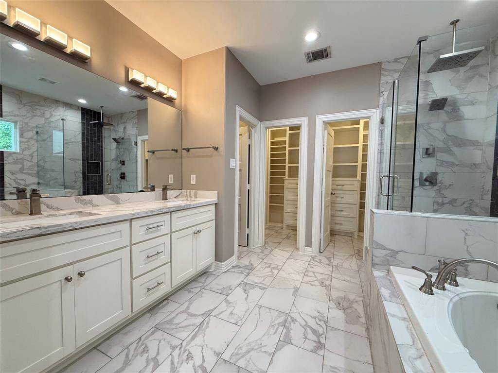 This spacious bathroom features elegant marble flooring, a large double vanity with ample storage, and a luxurious glass-enclosed shower. A soaking tub adds to the spa-like ambiance, and the walk-in closet offers generous space for clothes and accessories.