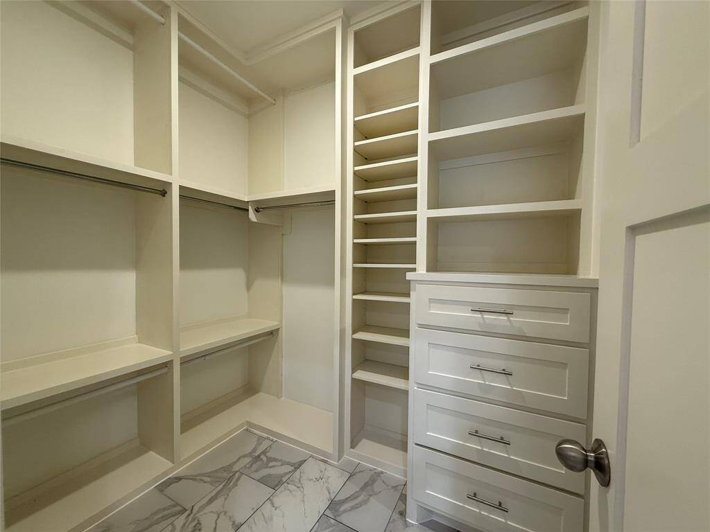 This is a spacious walk-in closet featuring custom shelving, multiple hanging rods, and built-in drawers, all with a sleek white finish. The floor is tiled with a marble-like pattern, adding a touch of elegance.