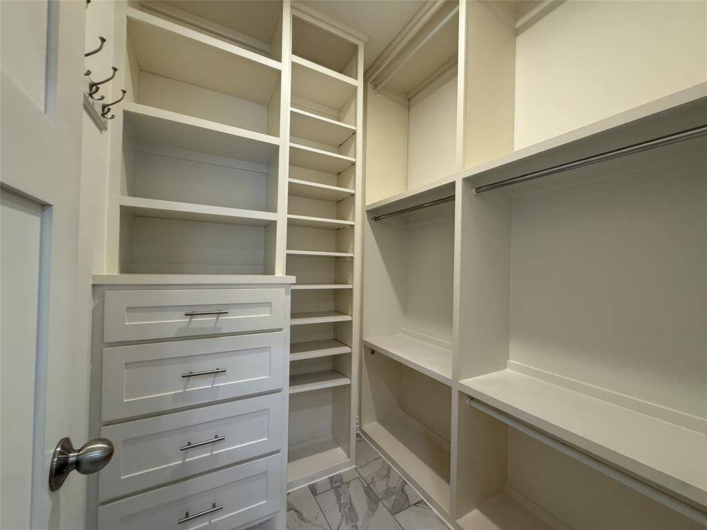 Spacious walk-in closet with ample shelving and hanging space, featuring elegant marble-tiled flooring and built-in drawers for organized storage.