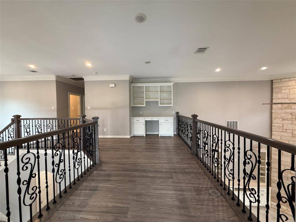 This photo showcases an upper-level landing with elegant wrought iron railings and hardwood flooring. The area includes built-in shelving and a desk, offering a versatile space for an office or reading nook. The neutral wall color complements the bright, open atmosphere.