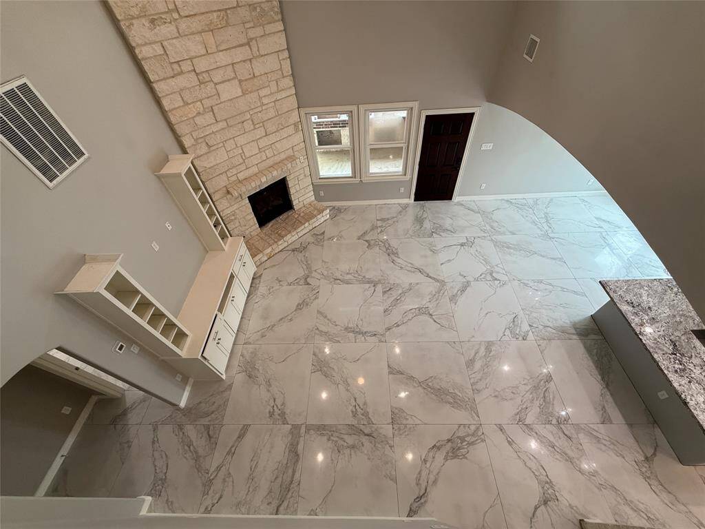 This spacious living area features marble-like tile flooring, a stone accent wall with a fireplace, built-in shelving, and abundant natural light from large windows. Perfect for modern living with an open and airy feel.
