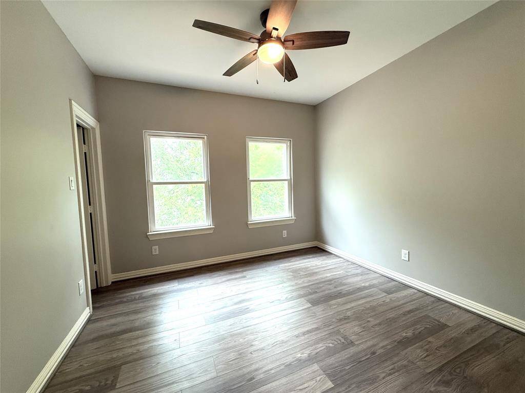 This room features two large windows for natural light, neutral-colored walls, wood-style flooring, and a ceiling fan, offering a cozy and modern space.