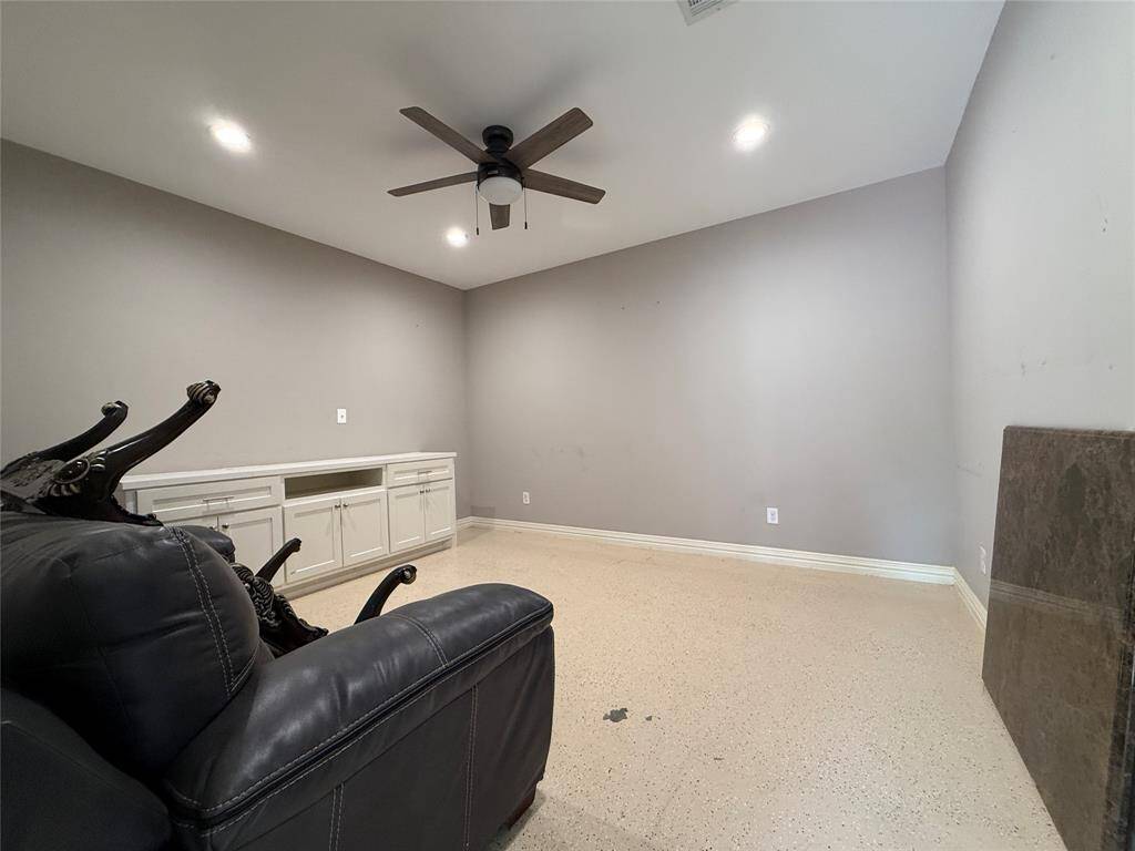This extra room in the back features neutral gray walls, a ceiling fan with light, and built-in cabinets. It has a spacious layout with a polished floor, ideal for a media or recreation room.