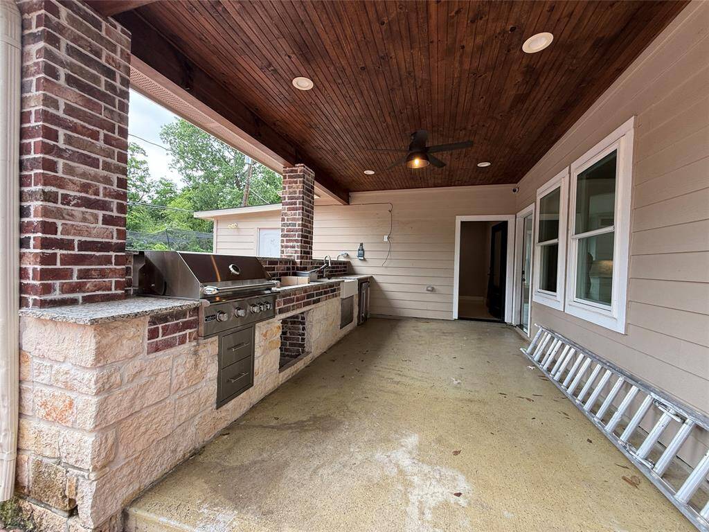 This photo showcases a covered outdoor kitchen with a built-in grill, brick and stone accents, and a wooden ceiling with recessed lighting and a fan. It's a great space for entertaining and outdoor cooking.