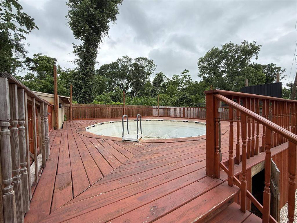 This photo features a spacious wooden deck surrounding an above-ground pool, offering a cozy outdoor area with lush greenery and privacy fencing. Ideal for relaxation and entertaining.