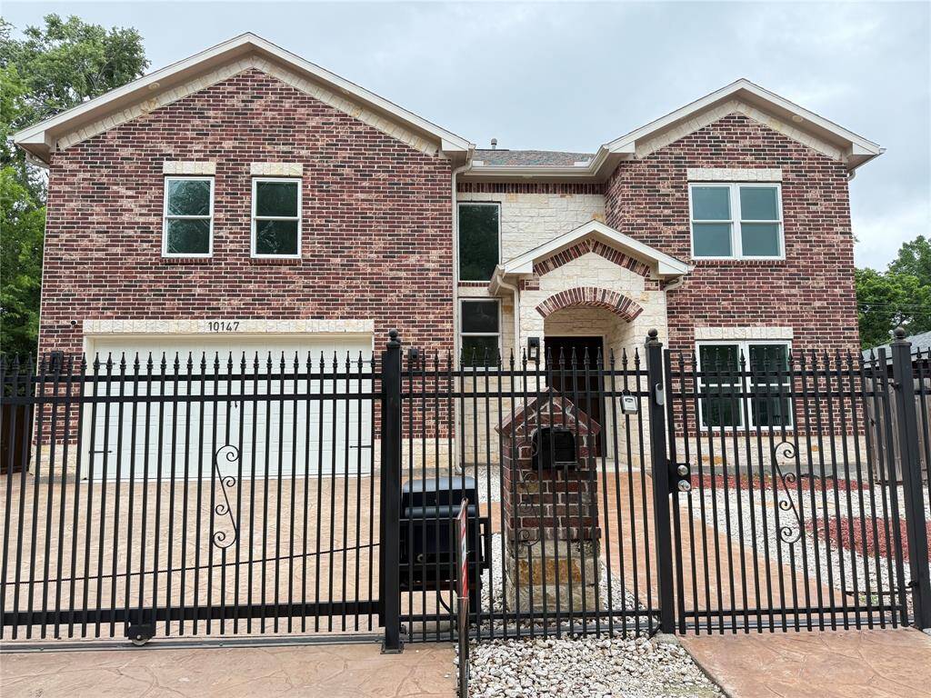 This photo shows a two-story brick house with a Two-car garage and a gated front yard. The exterior features a combination of red and light brickwork, with a paved driveway.