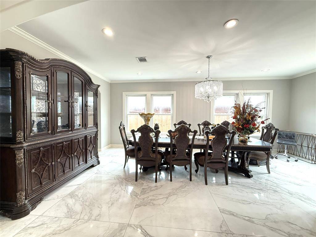 Elegant dining room with a large, ornate wooden table and chairs, a matching china cabinet, and a striking chandelier. The space is brightened by natural light from multiple windows, highlighting the glossy marble-like floor.
