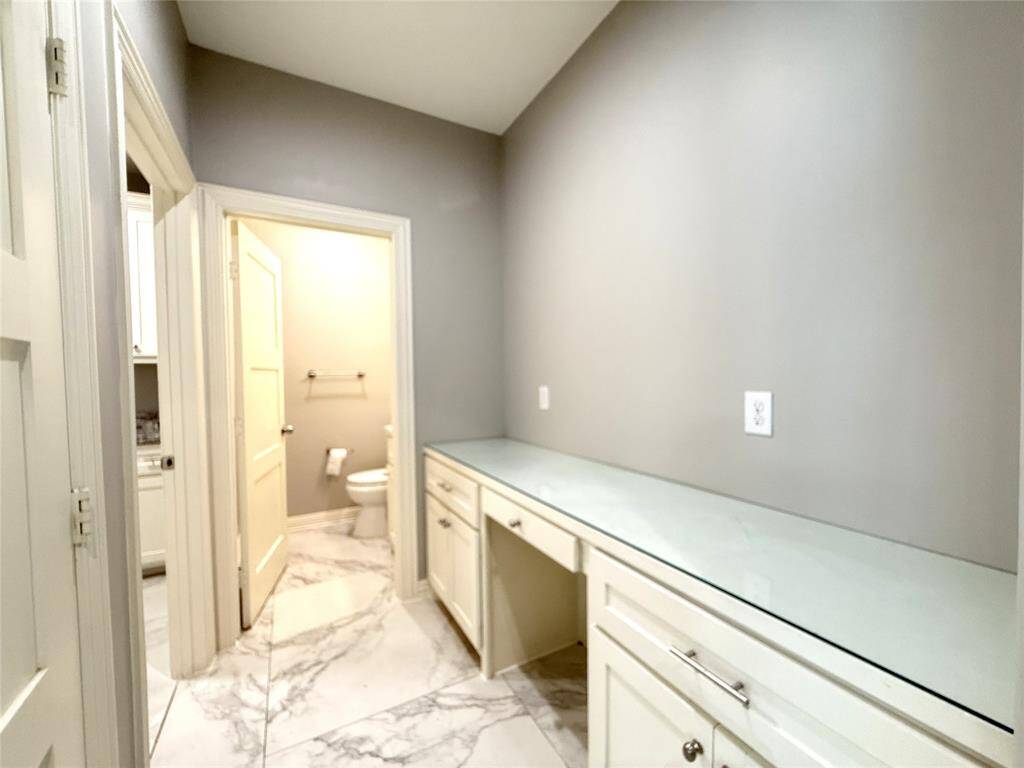 This photo features with sleek marble-like flooring and ample counter space. Adjacent is a half bathroom, adding convenience. The neutral color palette enhances the clean, modern feel.