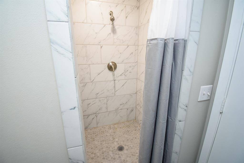 Walk-in shower with marble-style tiles and a pebble floor.