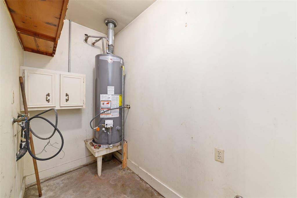 This photo shows a utility room with a water heater. It has white walls, some shelving for storage, and plumbing connections. The space appears functional and ready for use.
