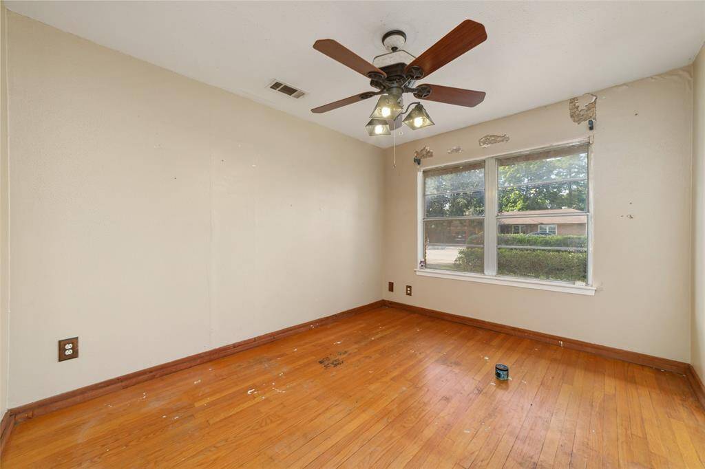 This room features hardwood flooring and a ceiling fan with lights. Large windows provide natural light, but the walls show some wear and need attention. It's a space with potential for customization.