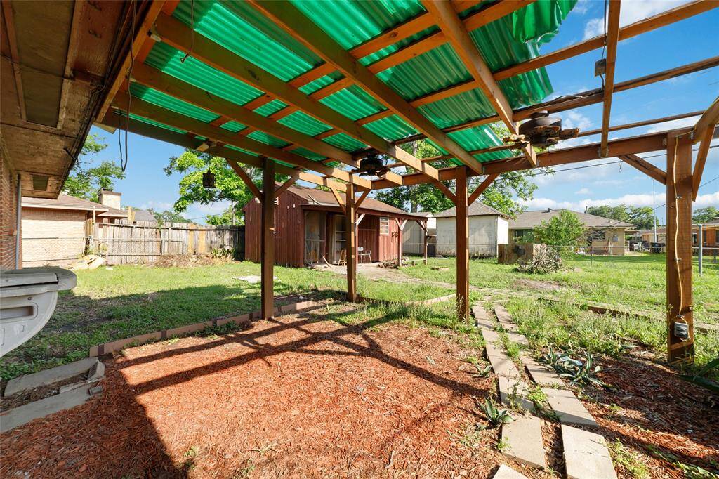 Charming backyard featuring a covered patio with a wooden pergola and green roofing. The spacious yard includes a shed and ample greenery, ideal for outdoor activities and gardening.