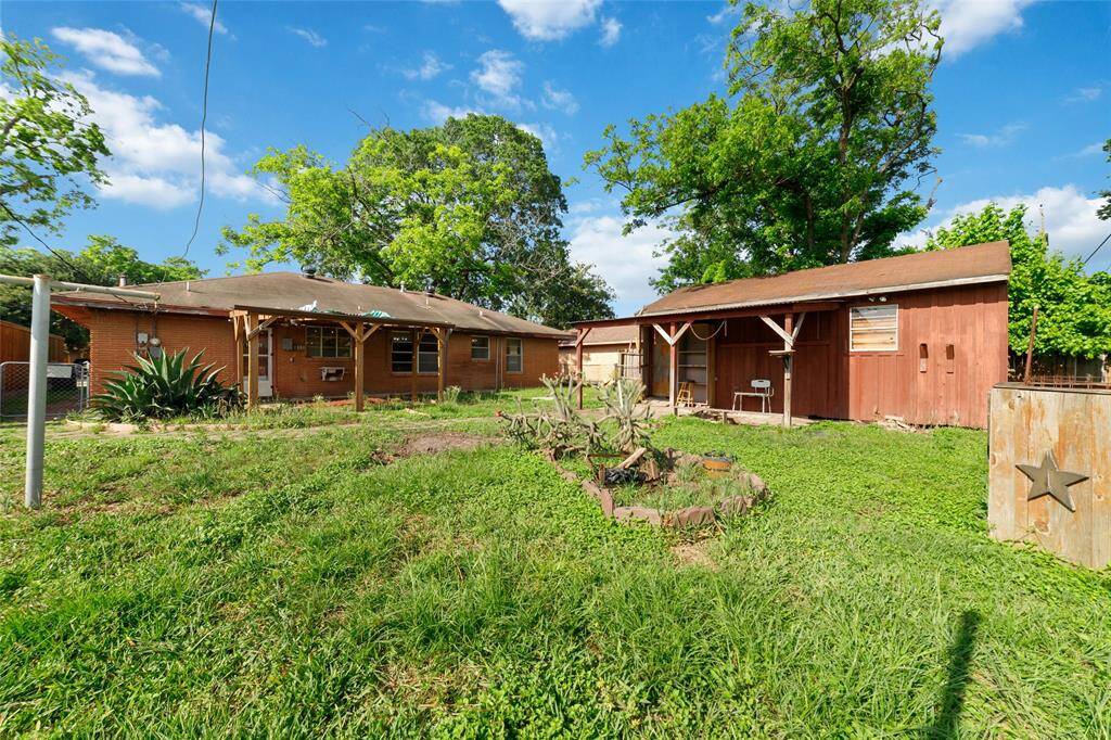 This photo showcases a spacious backyard with a lawn, mature trees, and a red wooden shed. The main house is brick with a covered patio, offering ample outdoor space for activities and storage.