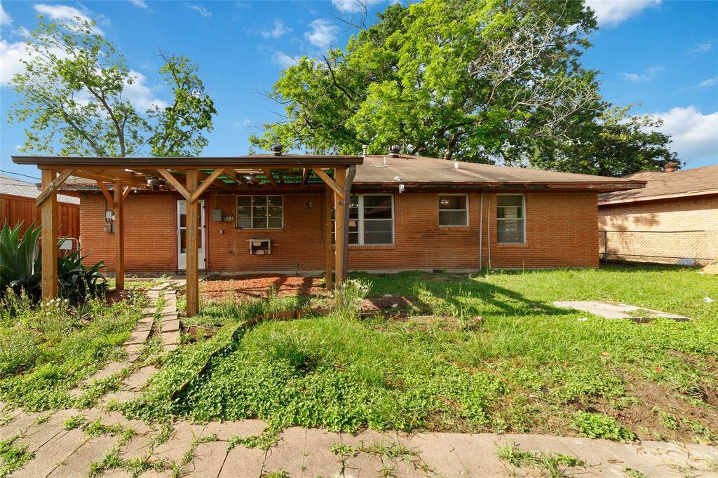 This backyard features a brick exterior, a wooden pergola, and a spacious grassy area, perfect for outdoor activities and relaxation.