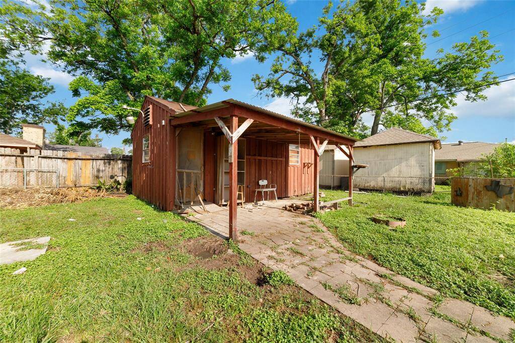 This photo showcases a rustic wooden shed in a spacious backyard. The shed features a small covered porch area and is surrounded by lush green grass and mature trees, offering a private and serene outdoor space.
