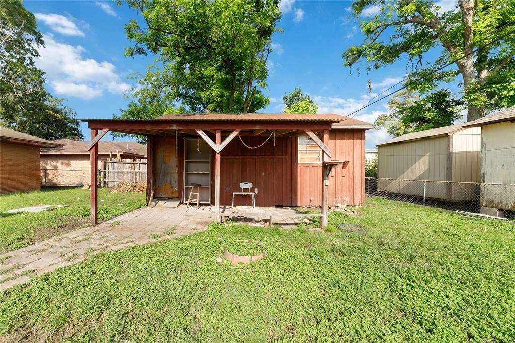 This photo features a backyard with a small wooden shed that has a covered porch area. The yard is grassy and partially fenced, offering potential for gardening or storage.