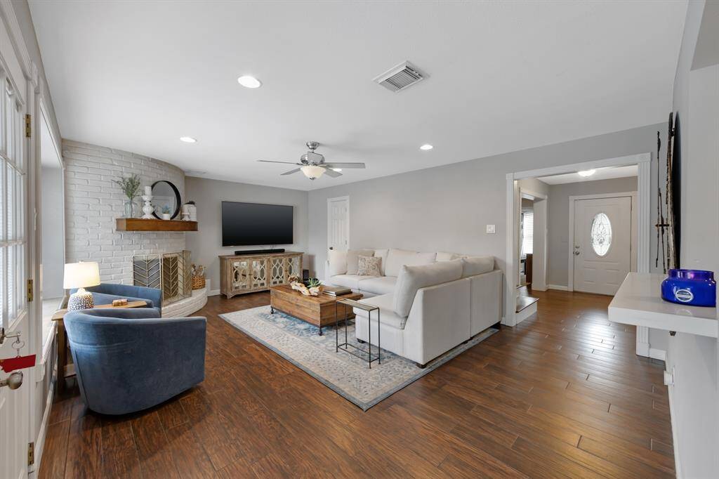 Open-concept layout leads directly into the spacious family room with soft light grey walls. Features include a charming bricked gas fireplace with a curved wood mantle as a cozy focal point.