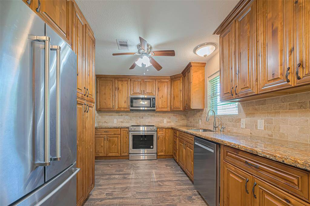 This kitchen features warm wood cabinetry (with tons of storage), stainless steel appliances, and granite countertops. It has a modern feel with a tile backsplash, ceiling fan, and ample natural light from window overlooking backyard