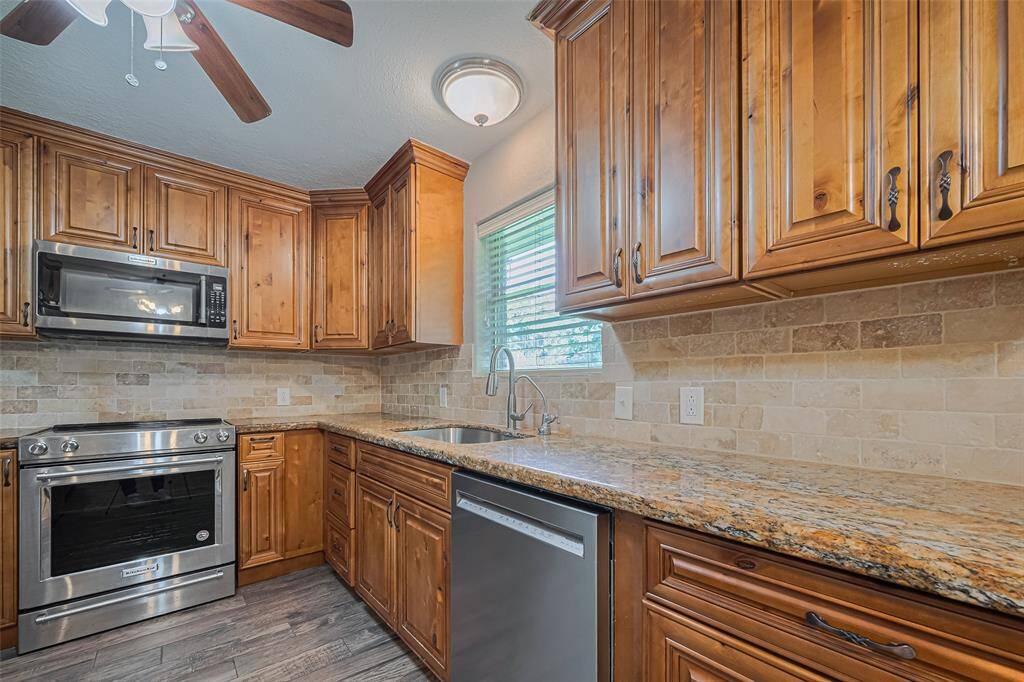 Updated kitchen offers pull out drawers, custom cabinets with soft close, stainless-steel appliances, and elegant granite countertops. Features a tile backsplash, a large sink, and ample natural light from the window, that overlooks the lush backyard