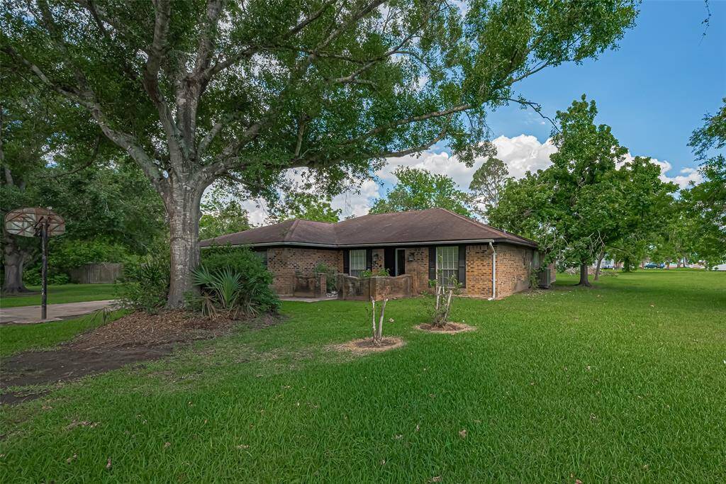 Charming single-story brick home surrounded by lush greenery and mature trees. The property features a well-maintained lawn and an inviting front entrance, ideal for a serene living environment.
