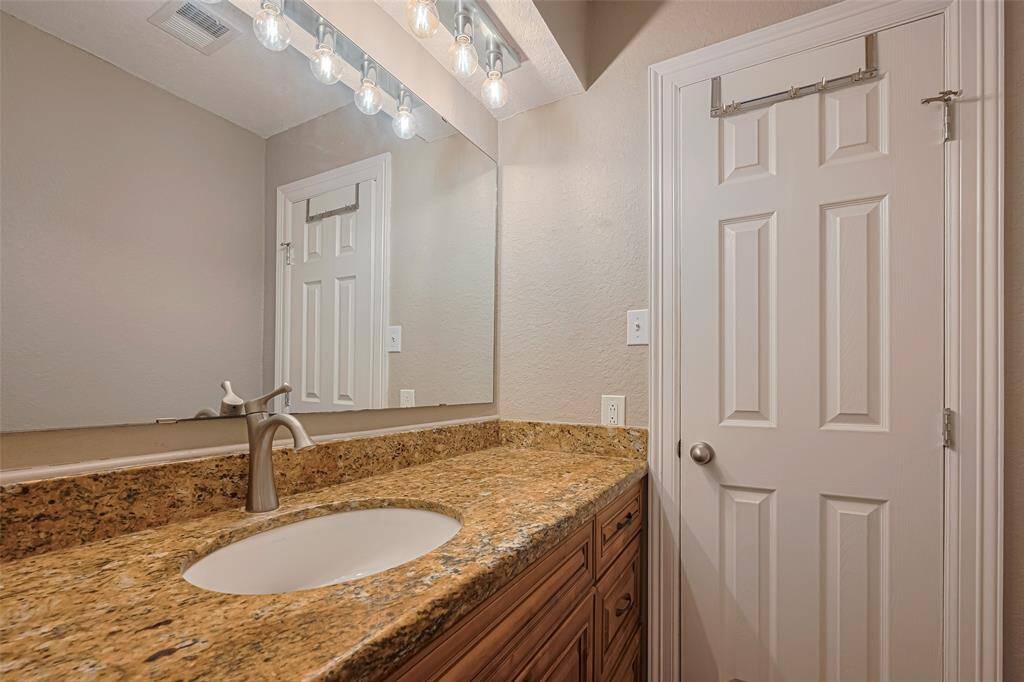 2nd bathroom features large granite vanity counters, custom lighting above large mirror, wood cabinets, and a tub/shower
