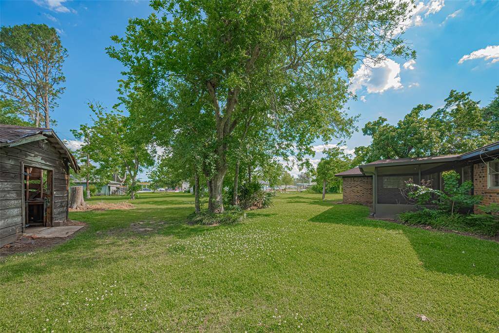 This photo shows a spacious, grassy backyard with mature trees providing shade. There's a rustic wooden shed and a screened porch on the side, offering potential for outdoor activities and storage. The area is open and well-maintained, perfect for enjoying nature.